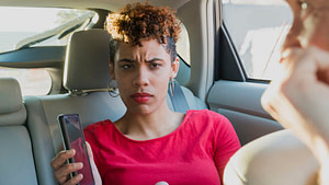 This is a passenger in a vehicle holding a smartphone. She looks angry. 