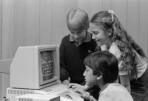 a black and white photo from the 1980's- three pre-teens gather around an old computer monitor to play Pacman. Teens Ditch the Phone?