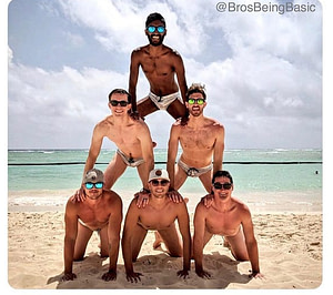 A photo of five boys forming a human pyramid. Photo taken at the beach. They are in swimsuits.